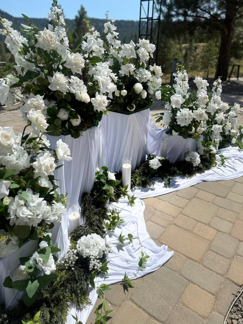 Close-up of 12-inch white pedestal rental with lush white roses and greenery at outdoor mountain wedding ceremony | Lake Tahoe & Reno