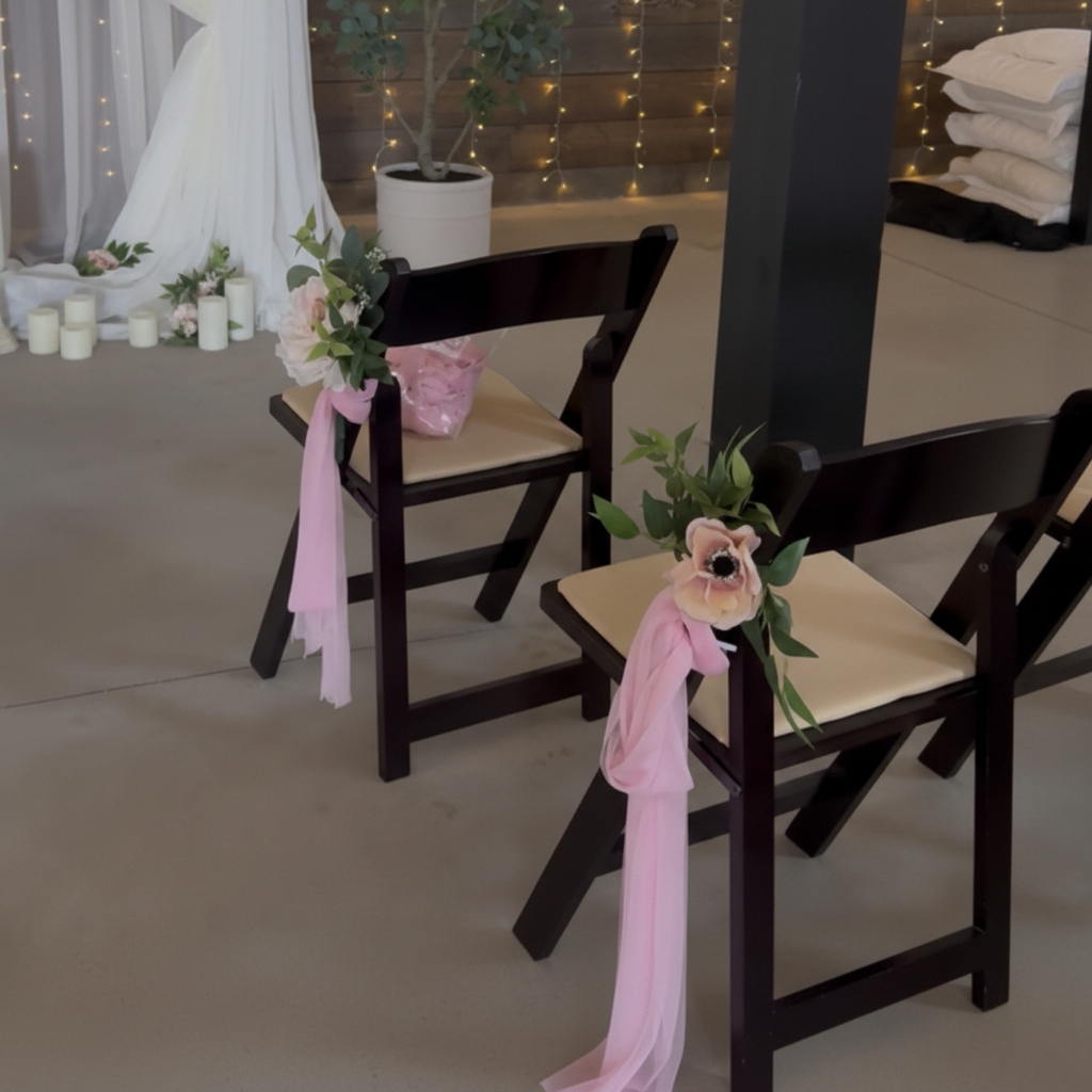 Pink Rose & Dahlia Aisle Chair Flower Rentals with blush pink rose and anemone clusters with lush green leaves tied with long flowing blush pink chiffon ribbons on dark wood folding wedding chairs at bright airy indoor wedding venue | Reno, Lake Tahoe & Sacramento