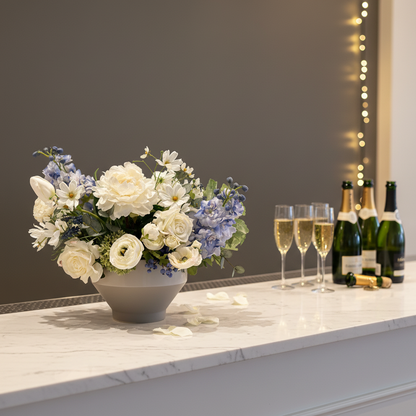 Blue Sunshine centerpiece rental with white peonies, blue hydrangea, blue delphinium, white garden roses, and white cosmos in gray bowl vase on elegant wedding bar top with warm lighting and champagne glasses in background | Reno, Lake Tahoe & Sacramento