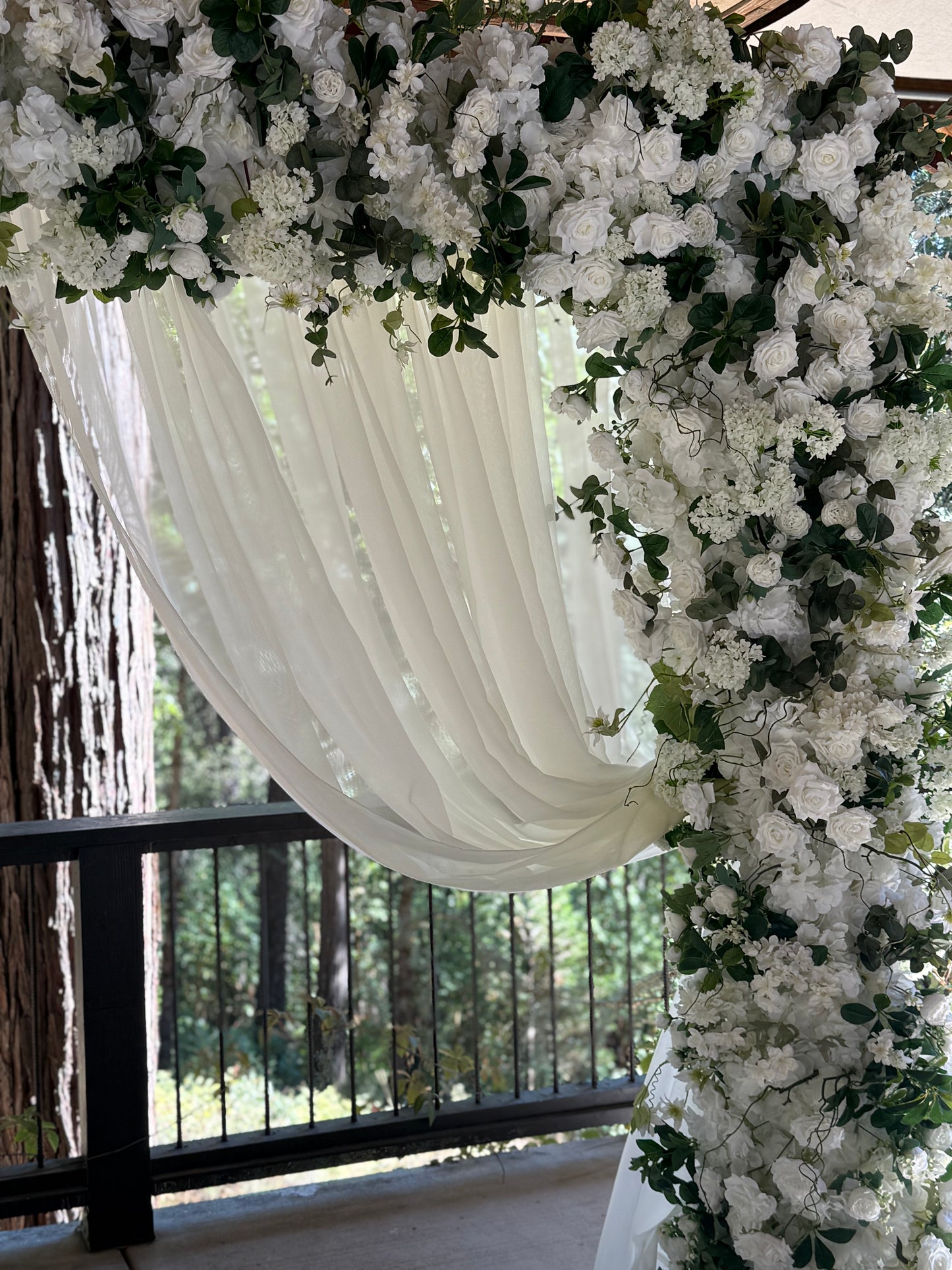 Close-up of Daydream arch rental top with white chiffon drapery and white roses, hydrangea, and greenery cascading over arch at outdoor redwood forest wedding | Reno, Lake Tahoe & Sacramento
