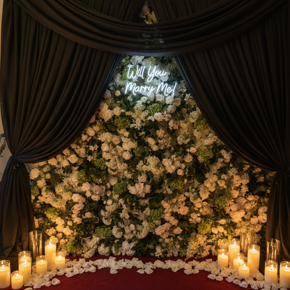 Light-Up LED "Will You Marry Me?" Sign Rental mounted on flowing black spandex drapery backdrop with white rose petals and candles at base in soft romantic lighting | Reno, Lake Tahoe & Sacramento