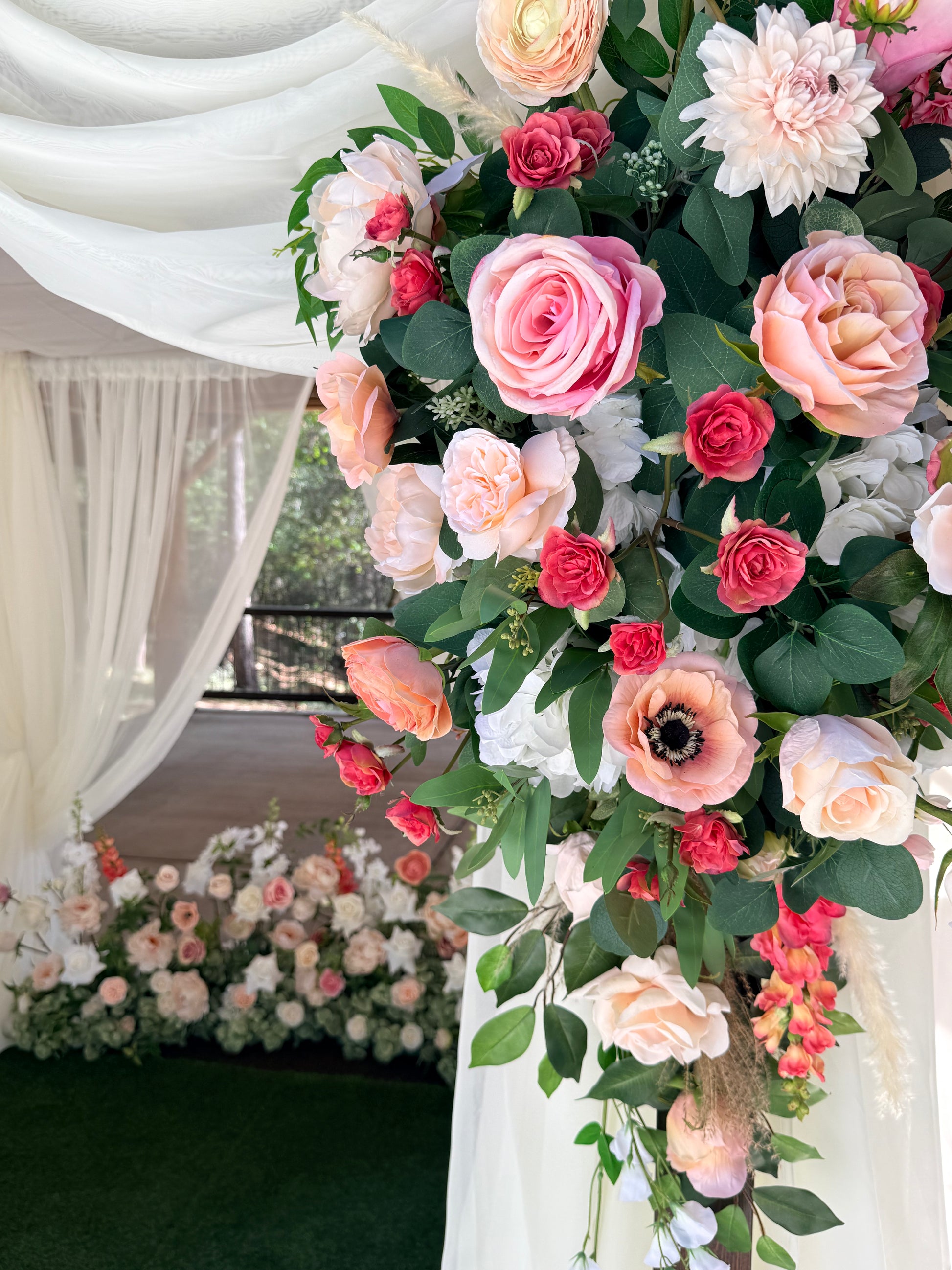 Close-up of Delicate arch adornment rental top corner with blush roses, snapdragons, ranunculus, and white drapery on rustic wood arch at outdoor forest wedding | Reno, Lake Tahoe & Sacramento
