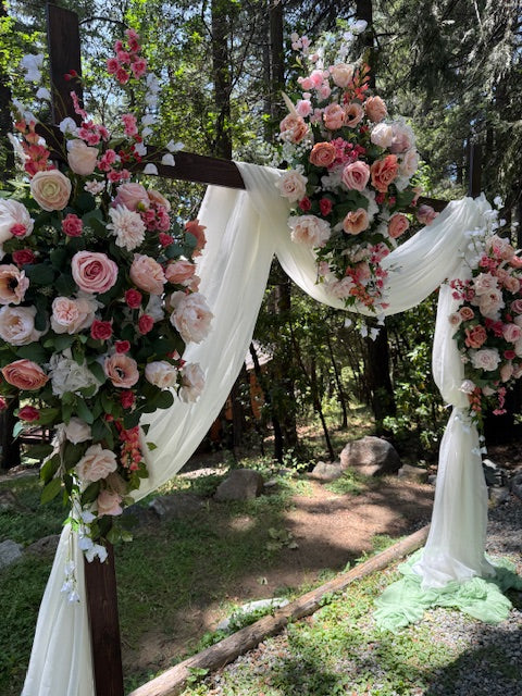 Delicate arch adornment rental with blush roses, ranunculus, and white drapery on rustic wood arch at outdoor forest wedding ceremony | Reno, Lake Tahoe & Sacramento