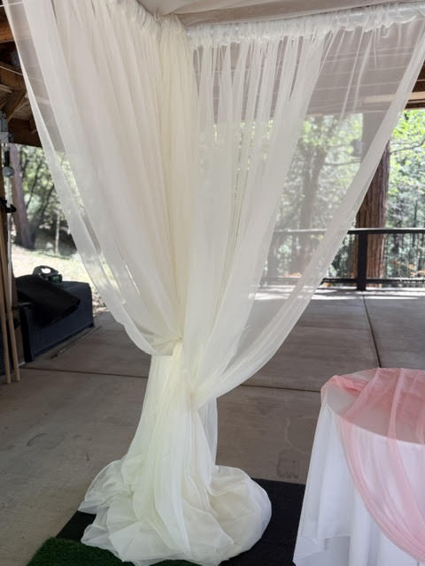Close-up detail of chuppah rental corner post with flowing white chiffon drapery pooling on ground at outdoor covered deck wedding venue with pine forest view | Reno, Lake Tahoe & Sacramento