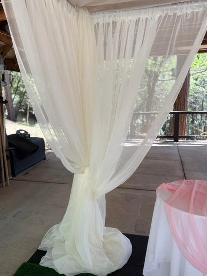 Close-up detail of chuppah rental corner post with flowing white chiffon drapery pooling on ground at outdoor covered deck wedding venue with pine forest view | Reno, Lake Tahoe & Sacramento
