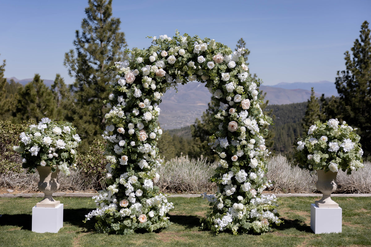Enchanted floral arch rental with white roses and greenery at outdoor garden wedding ceremony with white Enchanted urns on 12" pedestals | Reno, Lake Tahoe & Sacramento