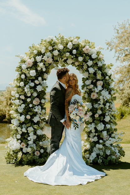 Enchanted floral arch rental fully covered in white and blush roses, peonies, hydrangea, and lush greenery at outdoor wedding venue | Reno, Lake Tahoe & Sacramento