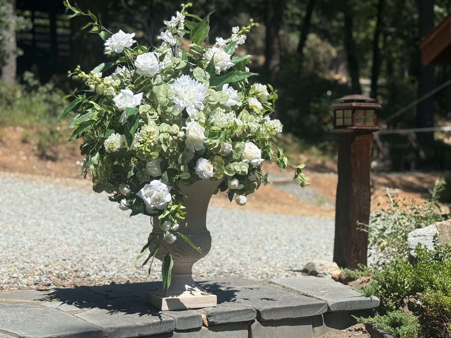 Enchanted floral stone urn rental with white roses, white dahlias, white hydrangea, and cascading greenery in dappled sunlight at outdoor pine forest wedding venue | Reno, Lake Tahoe & Sacramento