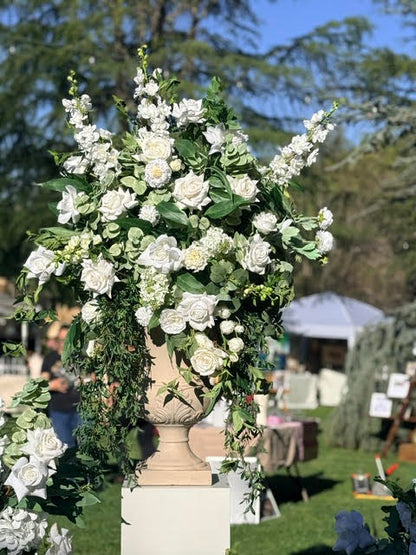 Enchanted floral stone urn rental on white pedestal overflowing with white roses, white delphinium, white hydrangea, and cascading greenery at outdoor wedding bridal market | Reno, Lake Tahoe & Sacramento