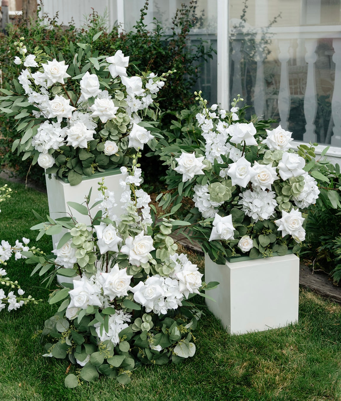 Two Enchanted aisle flower rentals on white square pedestals with white roses, white delphinium, white hydrangea, and lush eucalyptus at outdoor garden wedding venue with white pergola | Reno, Lake Tahoe & Sacramento