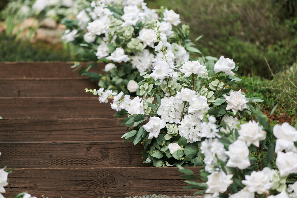 Close-up of Enchanted aisle flower rentals cascading down wood staircase with white roses, white gardenias, white hydrangea, and lush eucalyptus at outdoor wedding venue | Reno, Lake Tahoe & Sacramento
