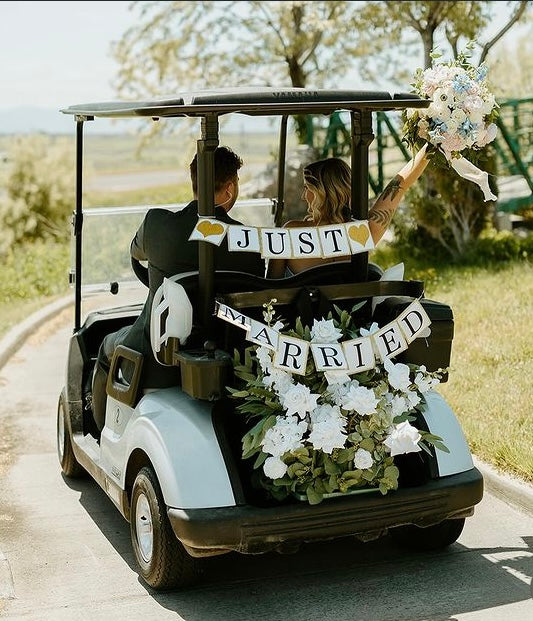 Bride and groom riding in golf cart decorated with Enchanted aisle flower rentals with white roses and lush greenery and Just Married banner at outdoor golf course wedding venue | Reno, Lake Tahoe & Sacramento
