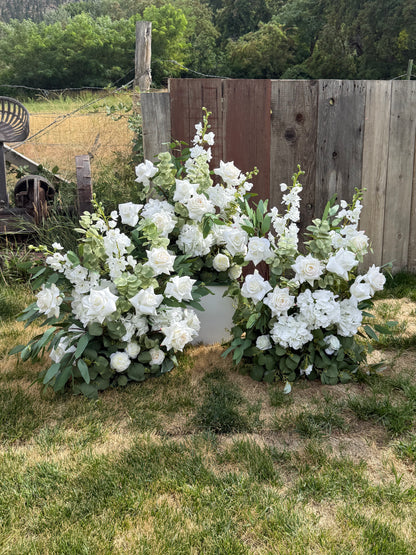 Three Enchanted aisle flower rentals on grass and 12" white pedestal with white roses, white delphinium, and lush greenery against rustic wood fence at outdoor wedding venue | Reno, Lake Tahoe & Sacramento