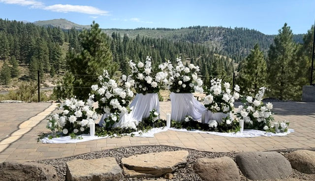 Enchanted aisle flower rentals styled with pedestals and fabric with white roses, white hydrangea, white delphinium, lush greenery, and pillar candles at outdoor mountain wedding venue with pine forest backdrop | Reno, Lake Tahoe & Sacramento