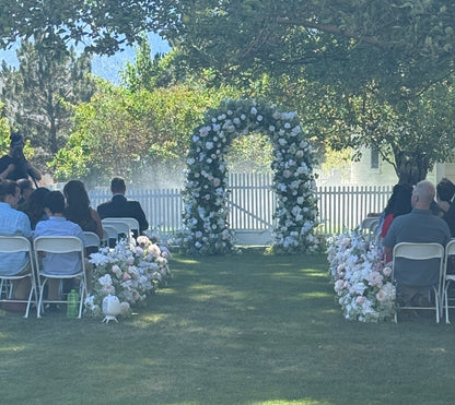 Live wedding ceremony with guests seated as Enchanted circular arch rental with white and peach roses and greenery stands at altar with Love Story aisle flowers lining outdoor garden venue | Reno, Lake Tahoe & Sacramento