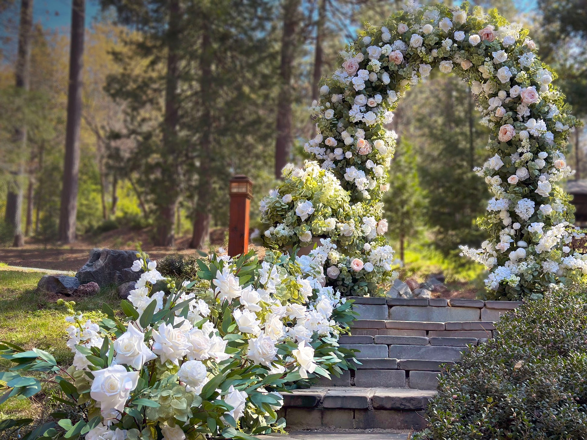 Enchanted circular arch rental with white roses, blush peonies, and greenery on stone steps at golden hour outdoor with Enchanted urns and aisle flowers in pine forest wedding venue | Reno, Lake Tahoe & Sacramento