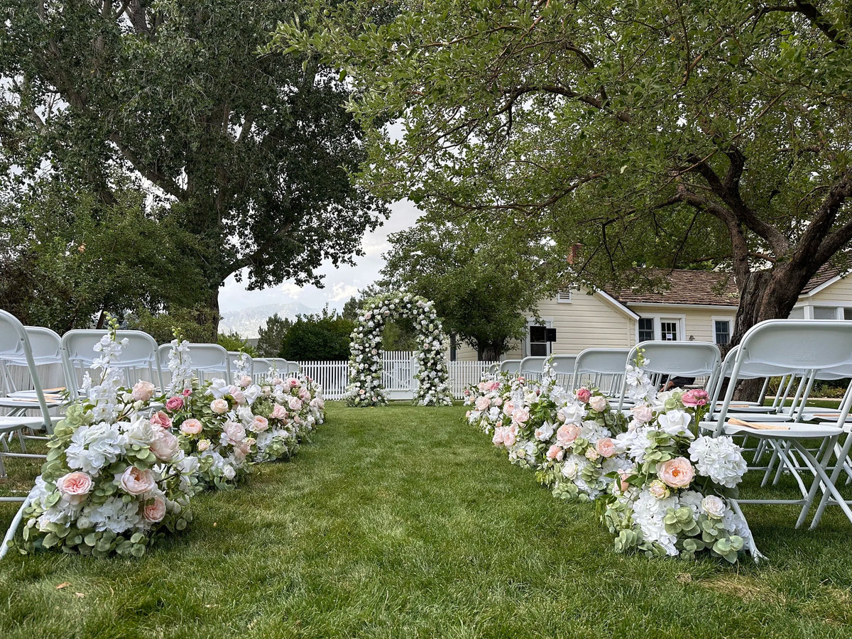 Love Story aisle flower rentals with blush, pink, and white roses and hydrangea lining outdoor grass ceremony aisle with Enchanted arch at altar and white folding chairs | Reno, Lake Tahoe & Sacramento
