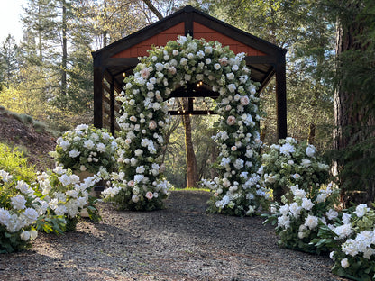 Enchanted circular arch rental with white and blush roses and greenery in front of wood pavilion at outdoor pine forest wedding venue with Enchanted aisle flowers and urns | Reno, Lake Tahoe & Sacramento