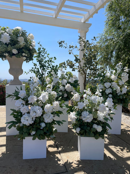 Multiple Enchanted aisle flower and urn rentals on white square pedestals under white pergola with white roses, white peonies, white delphinium, and lush eucalyptus with blue sky and valley view backdrop | Reno, Lake Tahoe & Sacramento