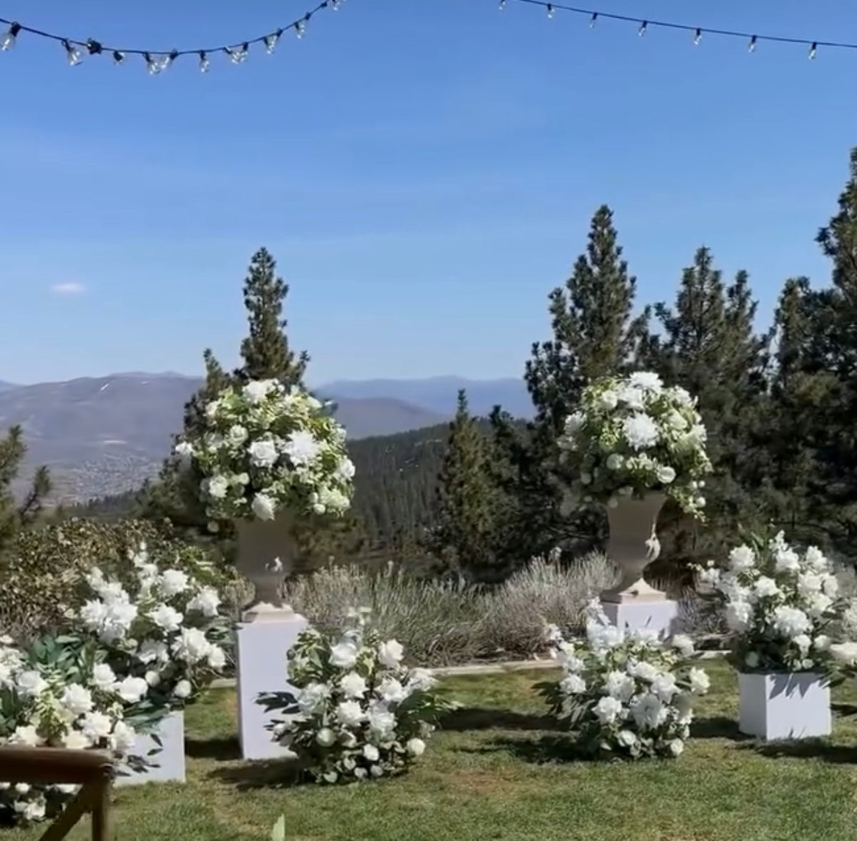 Enchanted aisle flower rentals on white square pedestals at outdoor mountain wedding venue with white roses, white hydrangea, and lush greenery with pine trees and blue sky backdrop | Reno, Lake Tahoe & Sacramento
