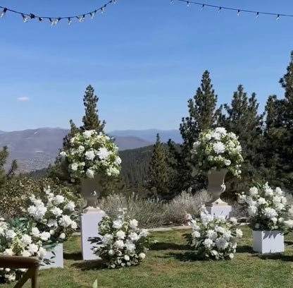Enchanted aisle flower rentals on white square pedestals at outdoor mountain wedding venue with white roses, white hydrangea, and lush greenery with pine trees and blue sky backdrop | Reno, Lake Tahoe & Sacramento