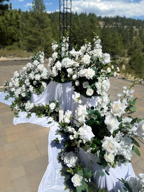 24-inch white pedestal rental draped in white fabric with cascading white roses, greenery, and candles at outdoor mountain wedding ceremony | Lake Tahoe & Reno