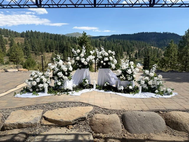 12-inch white pedestal rentals styled with white floral arrangements and drapery at outdoor mountain wedding ceremony with pine tree backdrop | Lake Tahoe & Reno