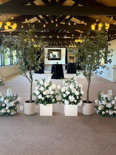 Close-up of two faux eucalyptus tree rentals and Enchanted ground florals used as a room divider between wedding ceremony and cocktail area with string lights overhead at indoor venue | Reno, Lake Tahoe & Sacramento