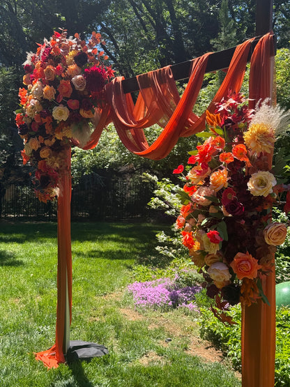 Full Evermore Fall arch adornment rental with coral roses, orange ranunculus, burgundy dahlias, and rust chiffon drapery at outdoor garden wedding venue | Reno, Lake Tahoe & Sacramento