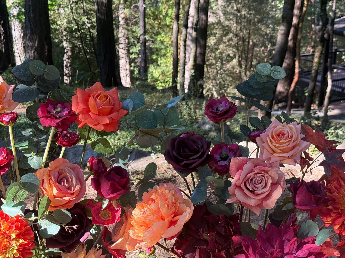 Close-up of Evermore Fall aisle flower rentals with coral, peach, and burgundy roses and eucalyptus in dappled sunlight at outdoor redwood forest wedding | Reno, Lake Tahoe & Sacramento