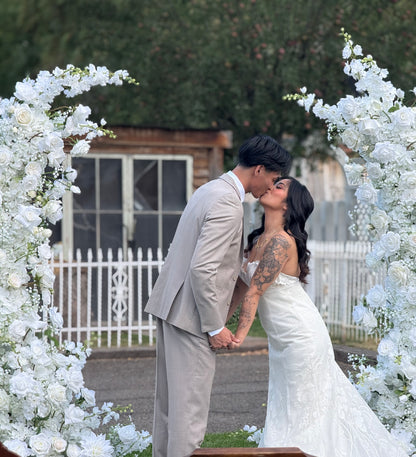 Bride and groom kissing framed inside Fairytale moon arch rental with white roses, baby's breath, and lush greenery at outdoor wedding venue | Reno, Lake Tahoe & Sacramento