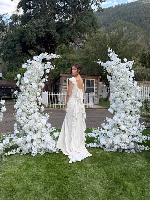 Bride standing between Fairytale double moon arch rentals fully covered in white roses, hydrangea, and lush greenery at outdoor mountain wedding venue | Reno, Lake Tahoe & Sacramento