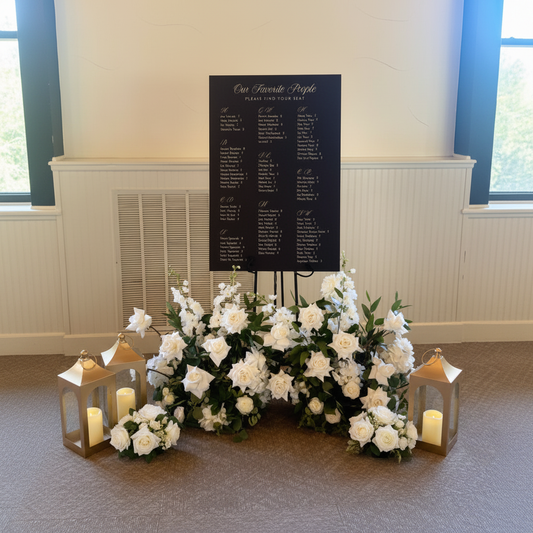 Golden Lantern Rentals set of 3 with glowing flameless pillar candles styled around an elegant black wedding seating chart sign on easel, two lanterns on the left and one on the right with small white rose centerpiece arrangements, soft warm venue lighting | Reno, Lake Tahoe & Sacramento