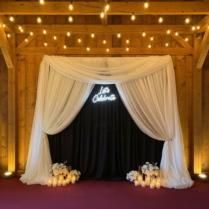 Light-Up LED "Let's Celebrate" Sign Rental mounted on flowing black spandex drapery backdrop with white florals and candles at base in rustic barn venue with warm wood walls and string lights | Reno, Lake Tahoe & Sacramento