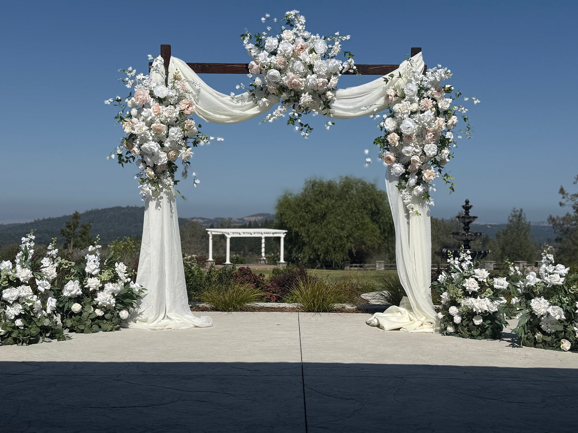 Full Love Story arch adornment rental with blush and white garden roses, delphinium, white drapery, and the lush Enchanted aisle flowers on rustic wood arch at outdoor hilltop wedding venue | Reno, Lake Tahoe & Sacramento