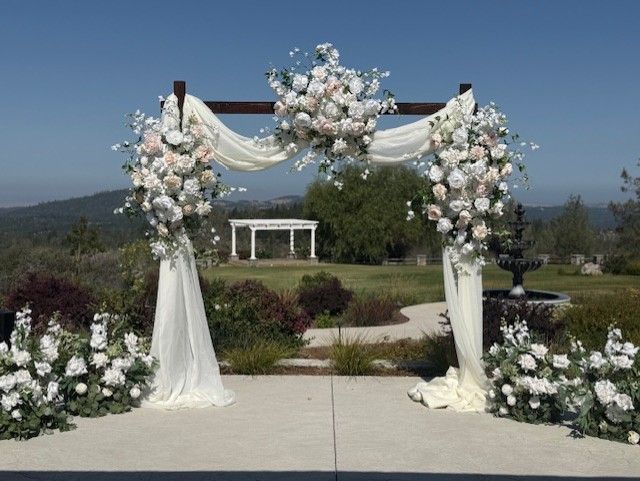 Wide view of Love Story arch adornment rental with blush and white garden roses, white drapery, and Enchanted aisle flower rentals at outdoor hilltop wedding venue with mountain and garden views | Reno, Lake Tahoe & Sacramento