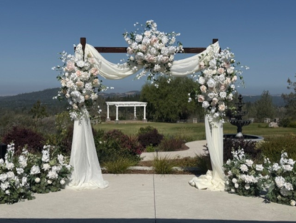 Wide view of Love Story arch adornment rental with blush and white garden roses, white drapery, and Enchanted aisle flower rentals at outdoor hilltop wedding venue with mountain and garden views | Reno, Lake Tahoe & Sacramento