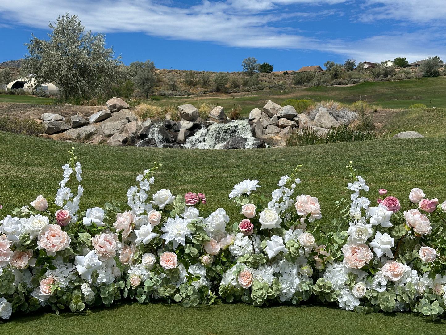 Love Story blush and white aisle flower rental displayed as ground floral installation at outdoor Reno Nevada wedding venue with waterfall backdrop | Reno, Lake Tahoe & Sacramento