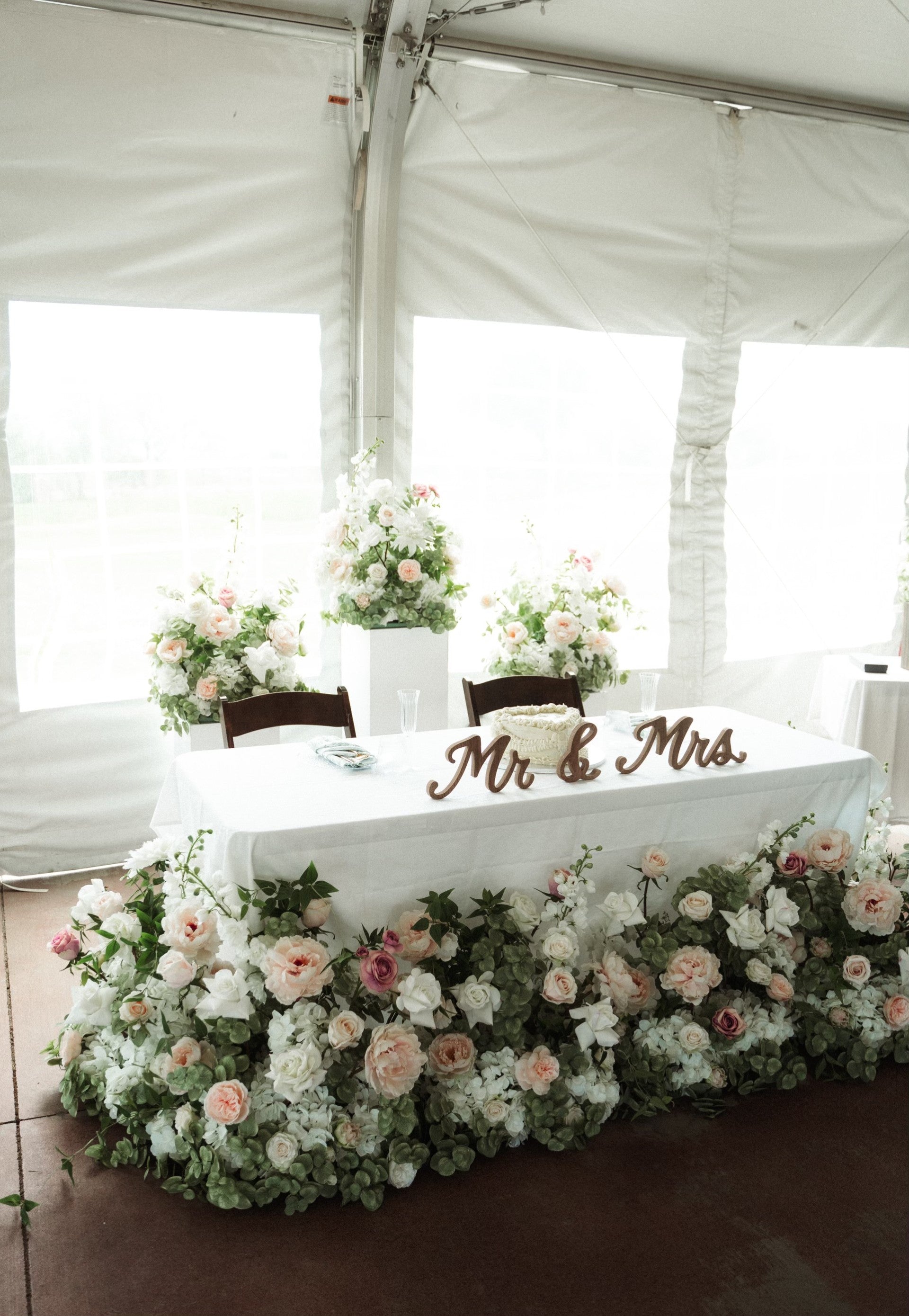 Mr & Mrs Wood Sign Rental on sweetheart table with Love Story aisle flower in lush blush and white floral table skirt of garden roses, hydrangea, and eucalyptus with tall white pedestals with more aisle flowers in elegant white tent wedding reception | Reno, Lake Tahoe & Sacramento 