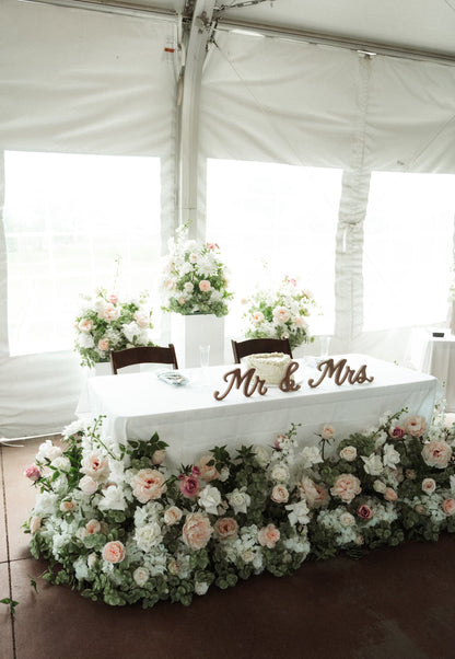 Mr & Mrs Wood Sign Rental on sweetheart table with Love Story aisle flower in lush blush and white floral table skirt of garden roses, hydrangea, and eucalyptus with tall white pedestals with more aisle flowers in elegant white tent wedding reception | Reno, Lake Tahoe & Sacramento 