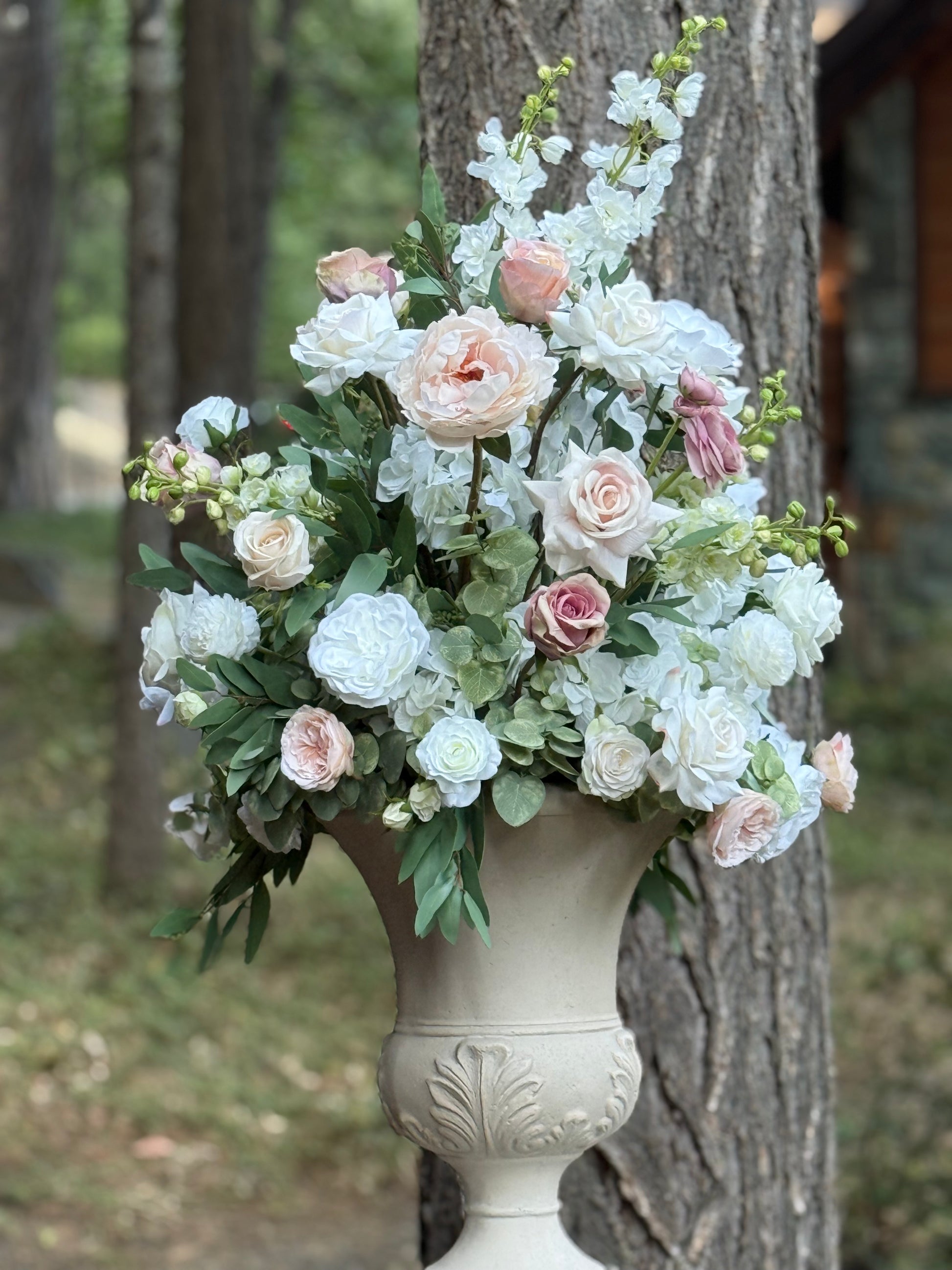 Love Story floral stone urn rental with white hydrangea, blush peonies, mauve roses, and white delphinium against pine tree at outdoor forest wedding venue | Reno, Lake Tahoe & Sacramento