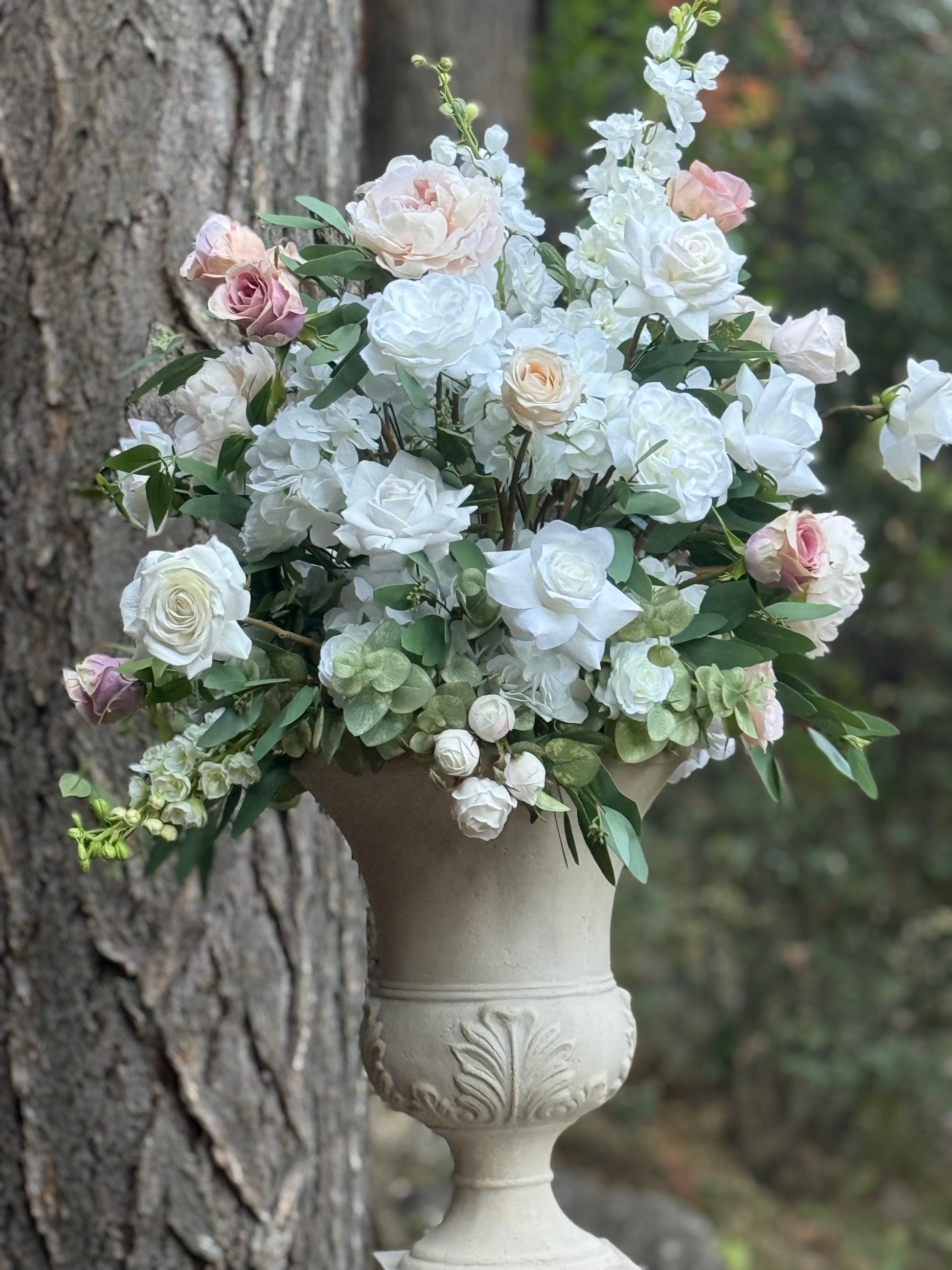 Love Story floral stone urn rental with white hydrangea, blush peonies, mauve roses, and white delphinium against pine tree at outdoor forest wedding venue | Reno, Lake Tahoe & Sacramento