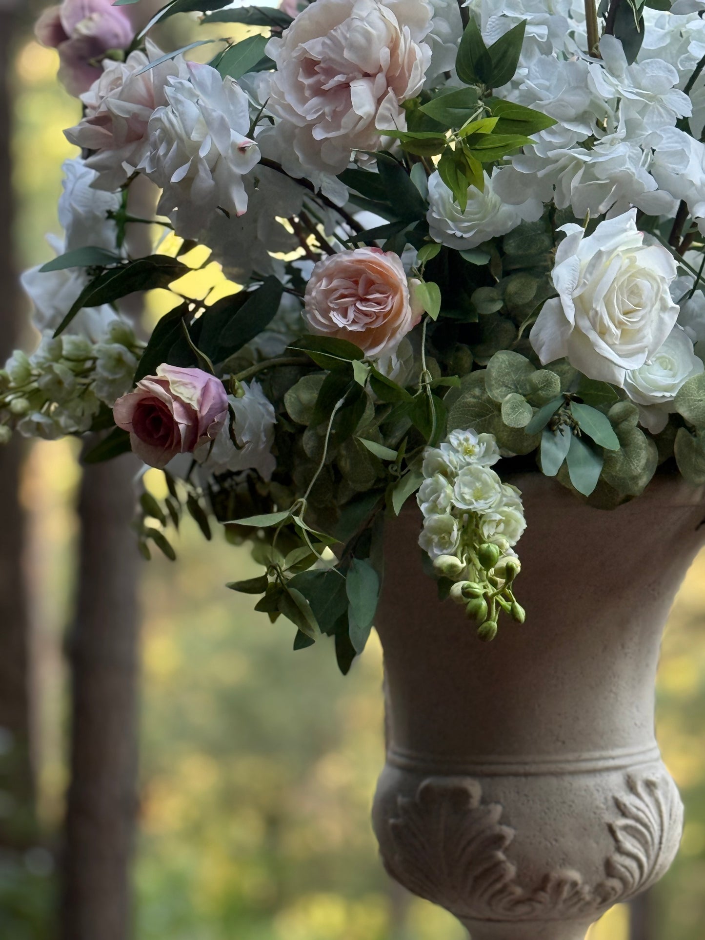 Close-up of Love Story floral stone urn rental with white garden roses, blush peonies, white delphinium, and lush greenery at outdoor pine forest wedding venue | Reno, Lake Tahoe & Sacramento
