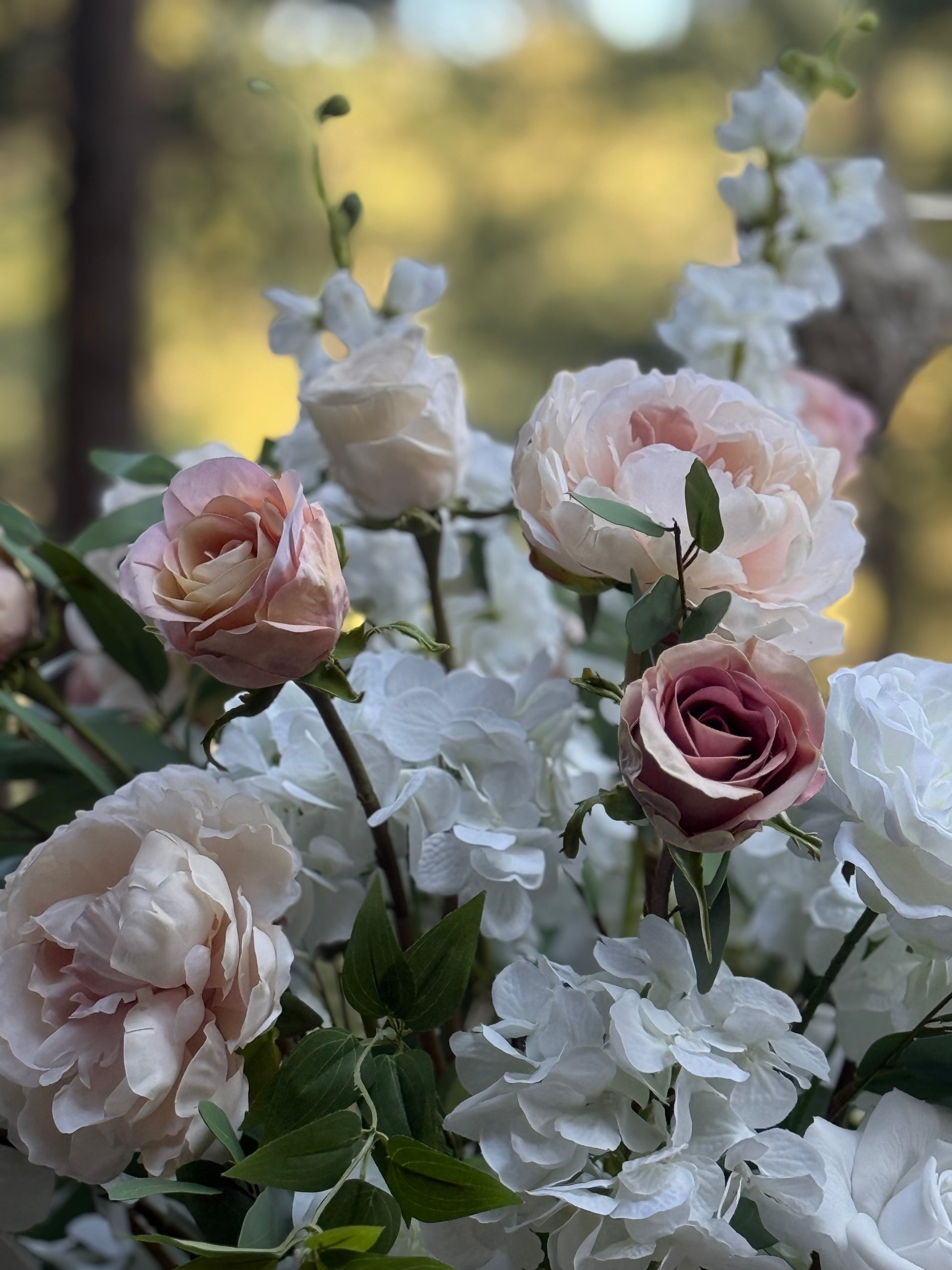 Close-up of Love Story floral stone urn rental overflowing with blush peonies, white hydrangea, cream roses, and cascading greenery at golden hour pine forest wedding venue | Reno, Lake Tahoe & Sacramento