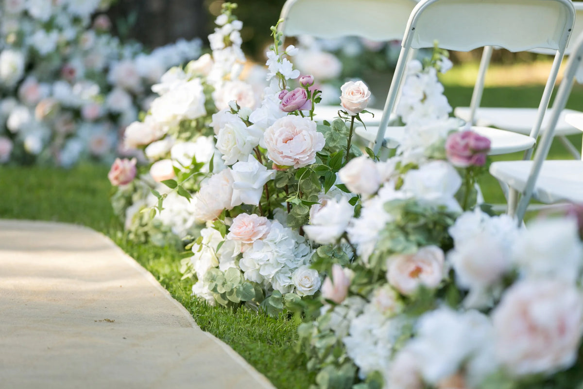Close-up of Love Story aisle flower rentals with blush, mauve, and white garden roses, hydrangea, and delphinium lining outdoor paved ceremony aisle beside white folding chairs | Reno, Lake Tahoe & Sacramento