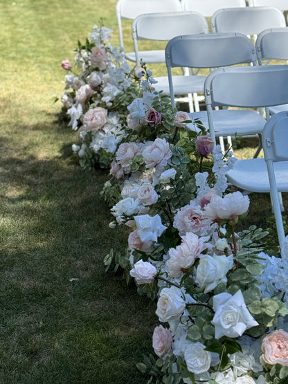 Side view of Love Story aisle flower rental row with blush, mauve, and white garden roses, peonies, and eucalyptus lining outdoor grass ceremony aisle beside white folding chairs | Reno, Lake Tahoe & Sacramento