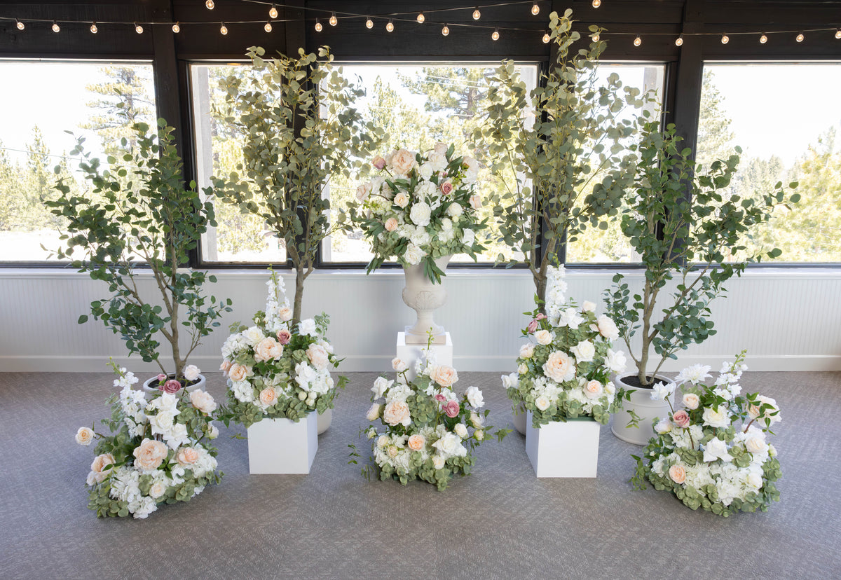 Love Story aisle flower rentals displayed with white pedestal, urns and faux eucalyptus trees at indoor Lake Tahoe wedding venue with string lights | Reno, Lake Tahoe & Sacramento