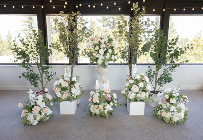 Love Story aisle flower rentals displayed with white pedestal, urns and faux eucalyptus trees at indoor Lake Tahoe wedding venue with string lights | Reno, Lake Tahoe & Sacramento