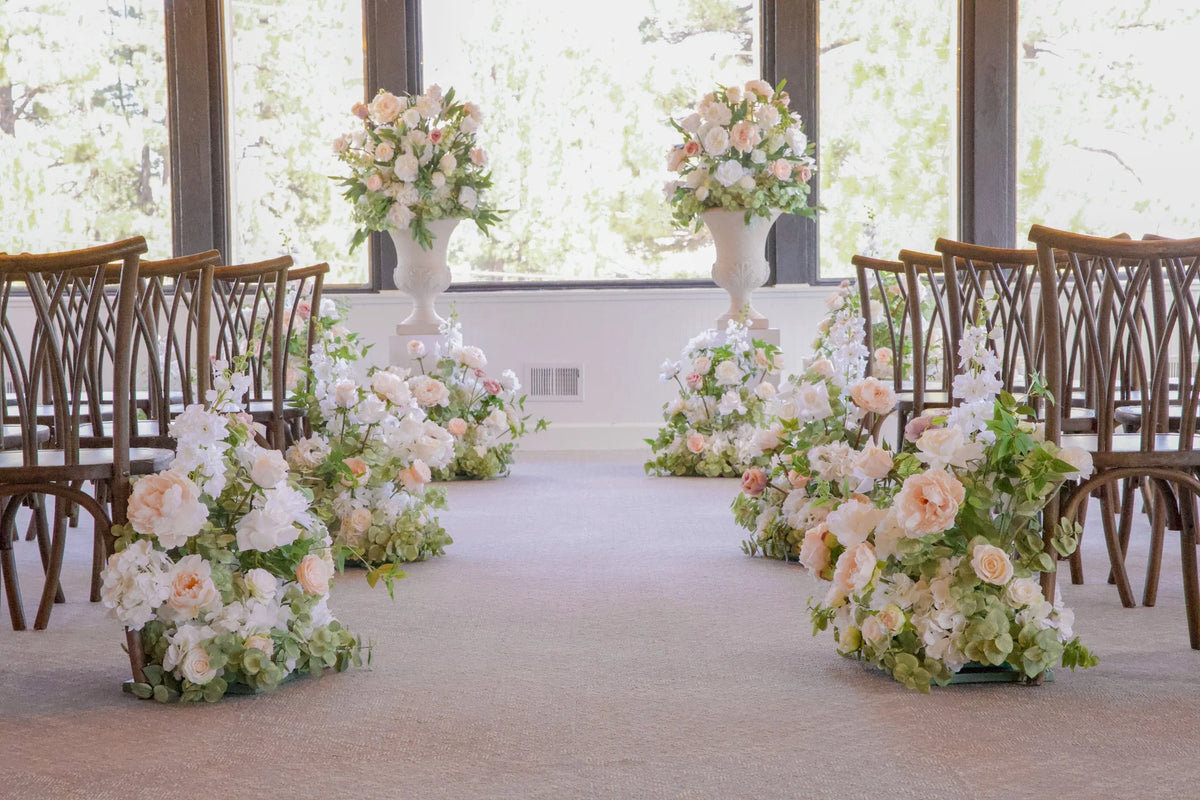 Love Story aisle flower rentals and white pedestals with urn rentals styling indoor ceremony aisle with blush, cream, and white roses, orchids, and hydrangea at Lake Tahoe wedding venue | Reno, Lake Tahoe & Sacramento
