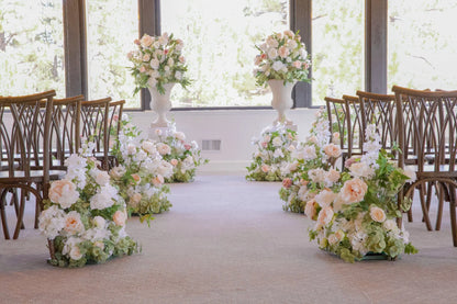 Love Story aisle flower rentals and white pedestals with urn rentals styling indoor ceremony aisle with blush, cream, and white roses, orchids, and hydrangea at Lake Tahoe wedding venue | Reno, Lake Tahoe & Sacramento